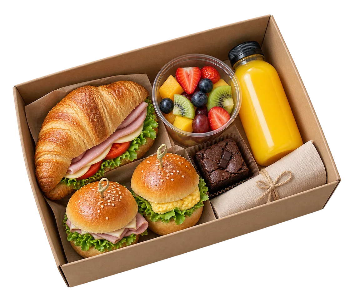 Ejemplo visual de un desayuno corporativo en caja con croissant, frutas, bebida y sándwiches